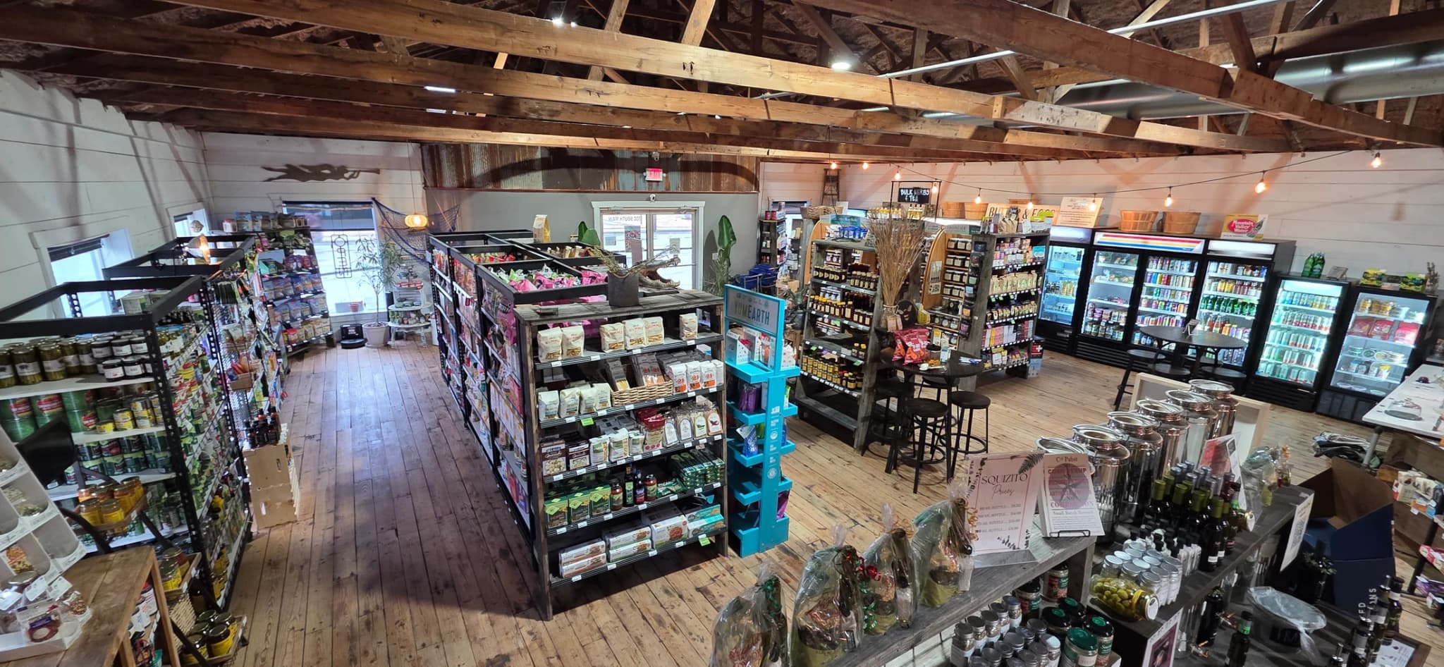 The grocery floor of the Natural Food Store, with stocked shelves and coolers under open timber trusses
