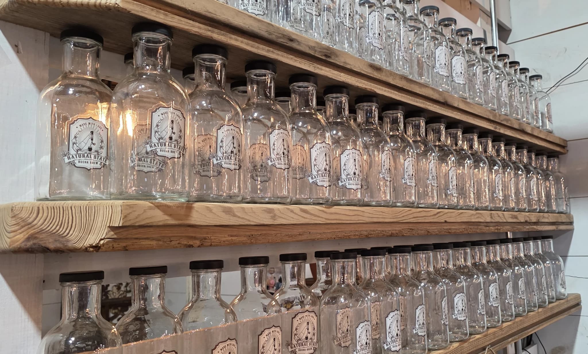 Shelves of Natural State Bucha Brew growler bottles